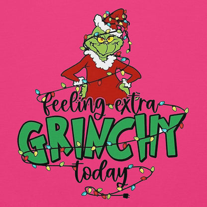 Cartoon character wearing a red suit with white fur trim and green hat, surrounded by Christmas lights on a pink background with text 'Feeling extra Grinchy today'.