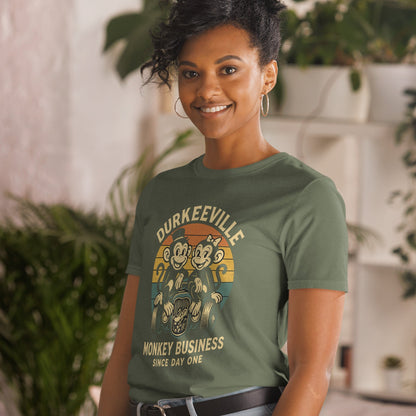 Woman wearing a green t-shirt with 'Durkeeville Monkey Business' design in an indoor setting.