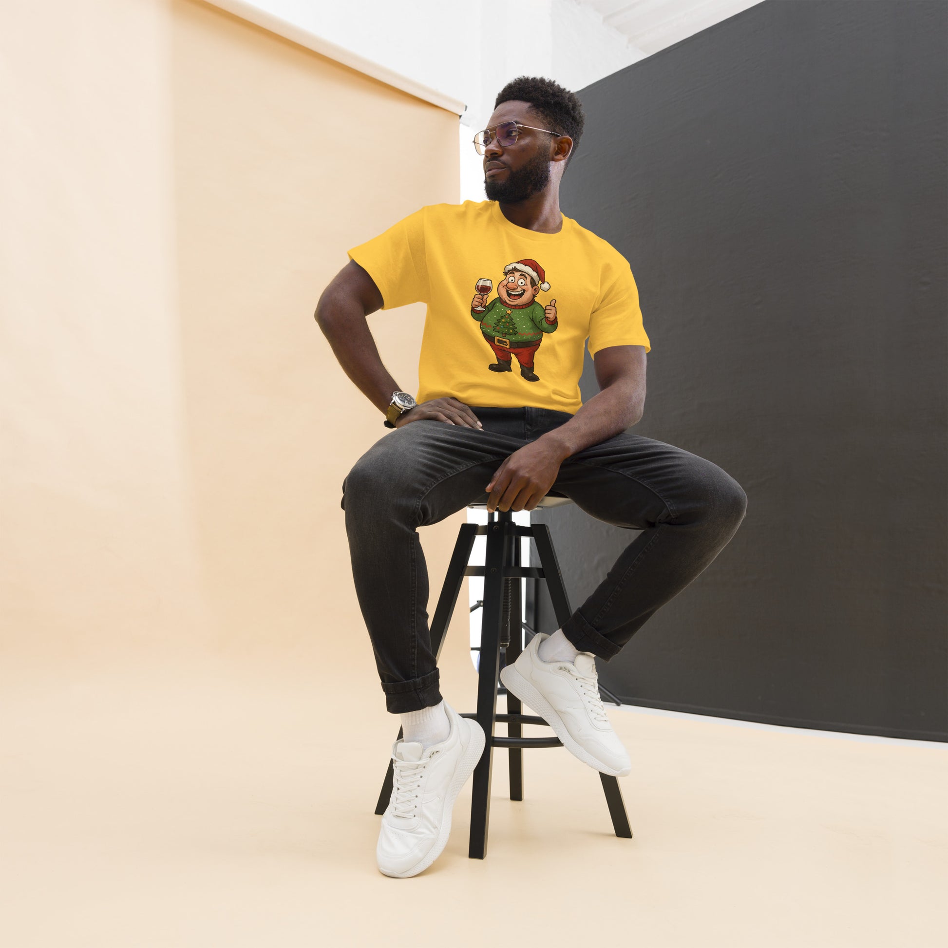 Man sitting on a stool wearing a yellow t-shirt with a graphic design, black pants, and white sneakers.