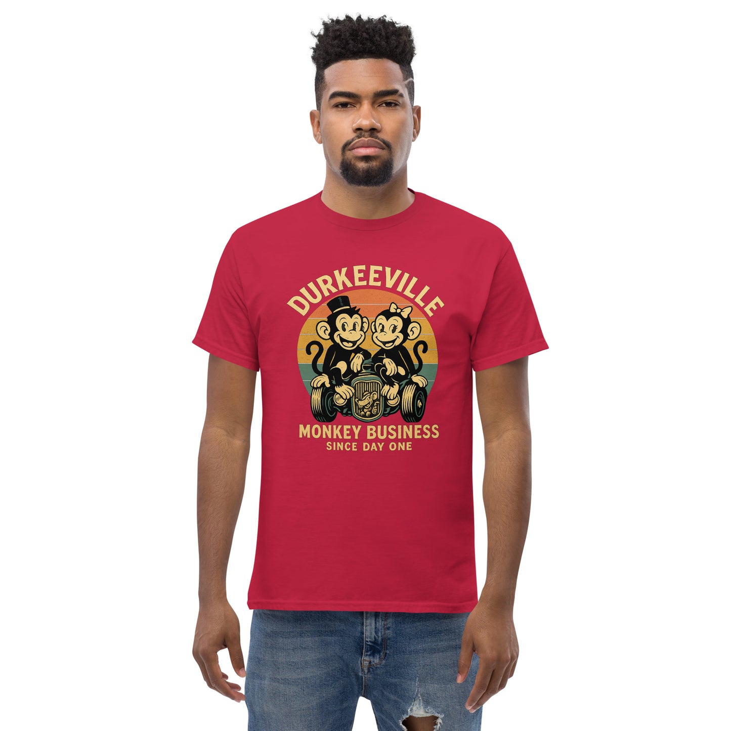 Man wearing a red t-shirt with 'Durkeeville Monkey Business Since Day One' graphic design.