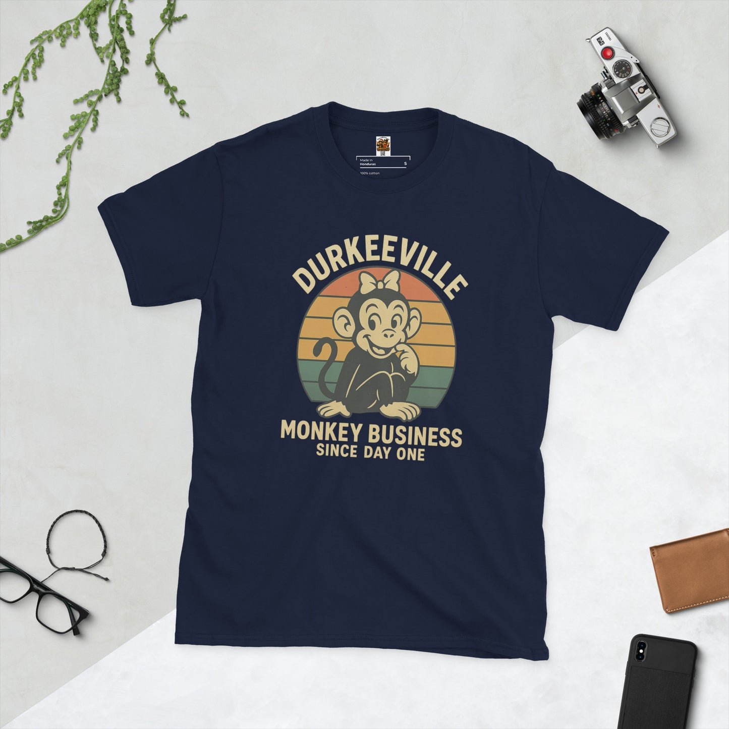 Navy blue t-shirt with a graphic design on a light gray surface with accessories around.