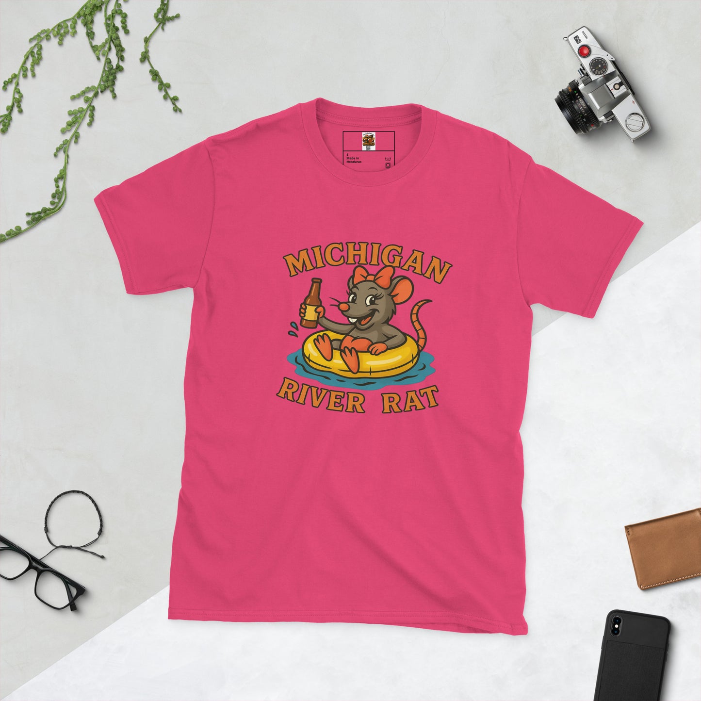 Pink t-shirt with 'Michigan River Rat' graphic on a light gray surface with accessories.