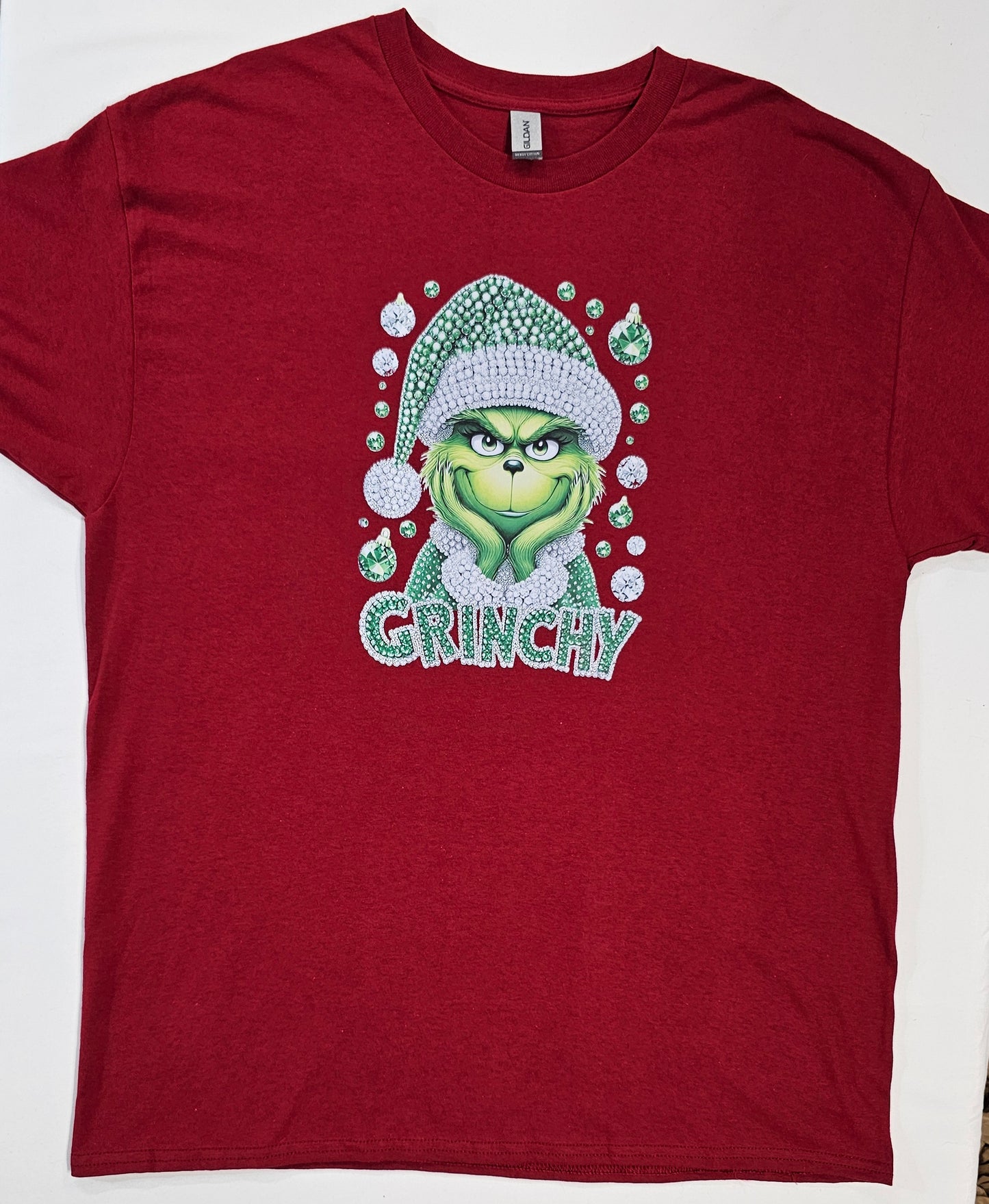 Red t-shirt with a graphic of a green character wearing a Santa hat and the word 'GRUNCHY' on a white background.