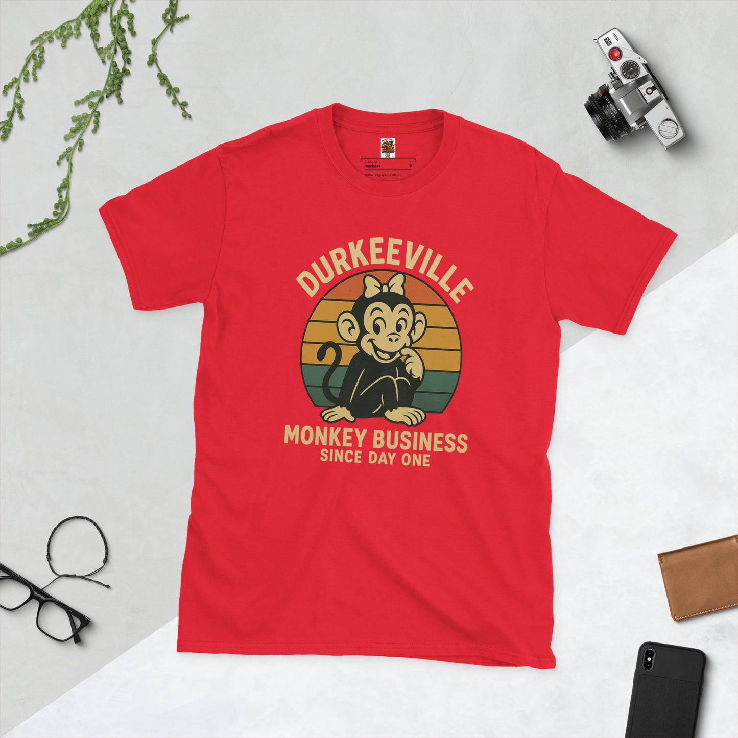 Red t-shirt with 'Durkeeville Monkey Business Since Day One' graphic on a light gray background.