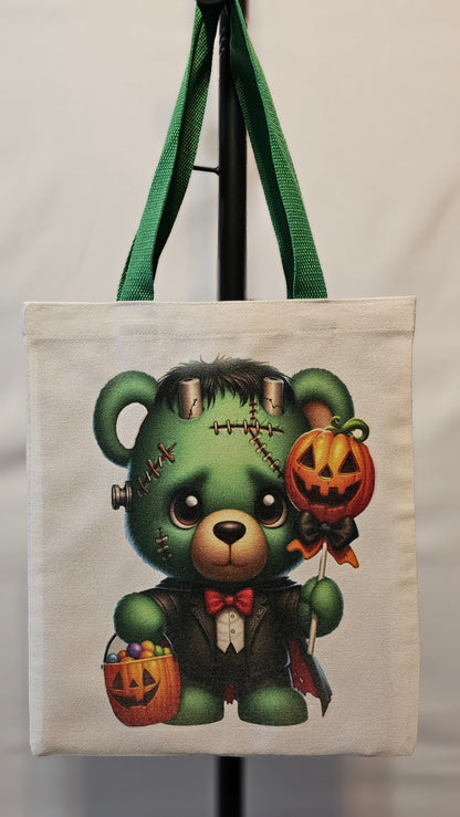 Tote bag with a green teddy bear design featuring Halloween elements on a white background.
