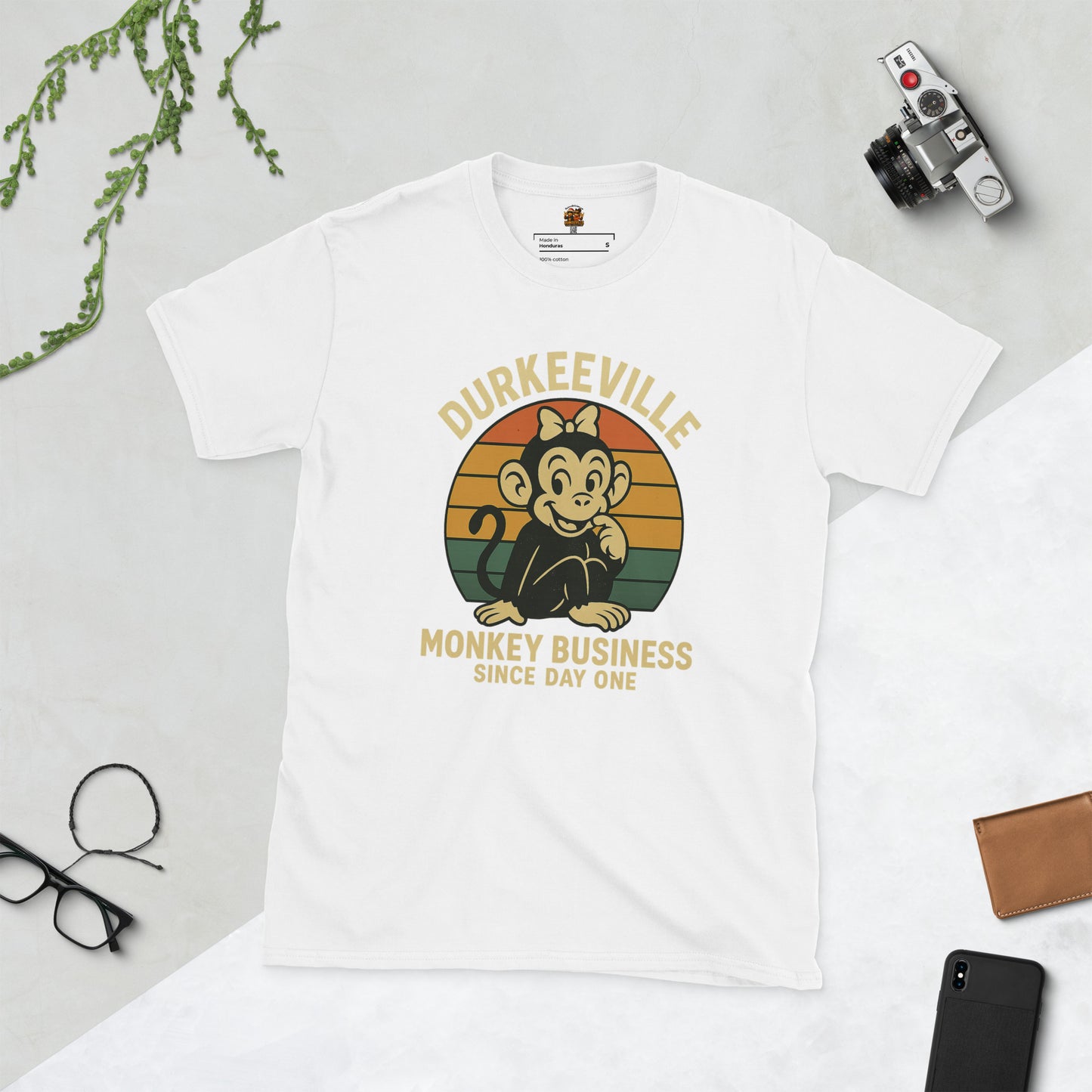 White t-shirt with 'Durkeeville Monkey Business Since Day One' graphic on a light gray background.