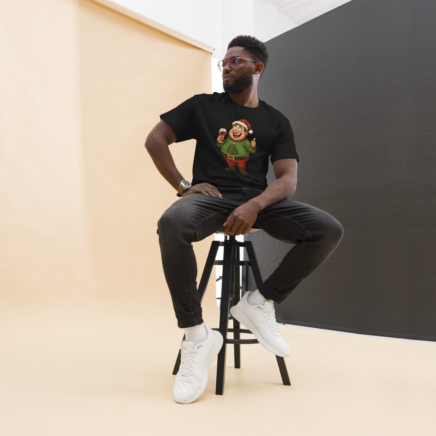 Man sitting on a stool wearing a black t-shirt with a graphic design, black pants, and white sneakers.