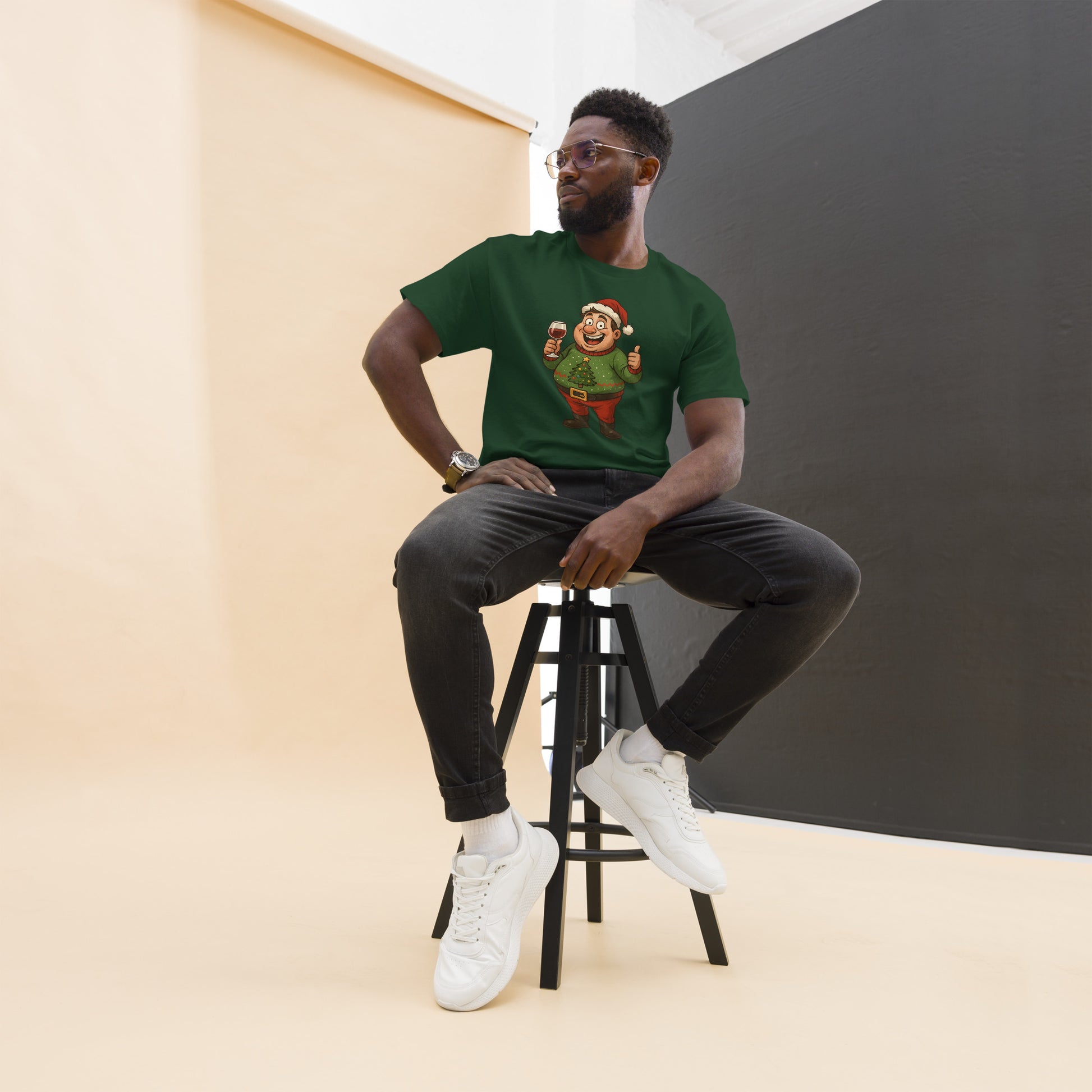 Man sitting on a stool wearing a green t-shirt with a graphic design, black pants, and white sneakers.