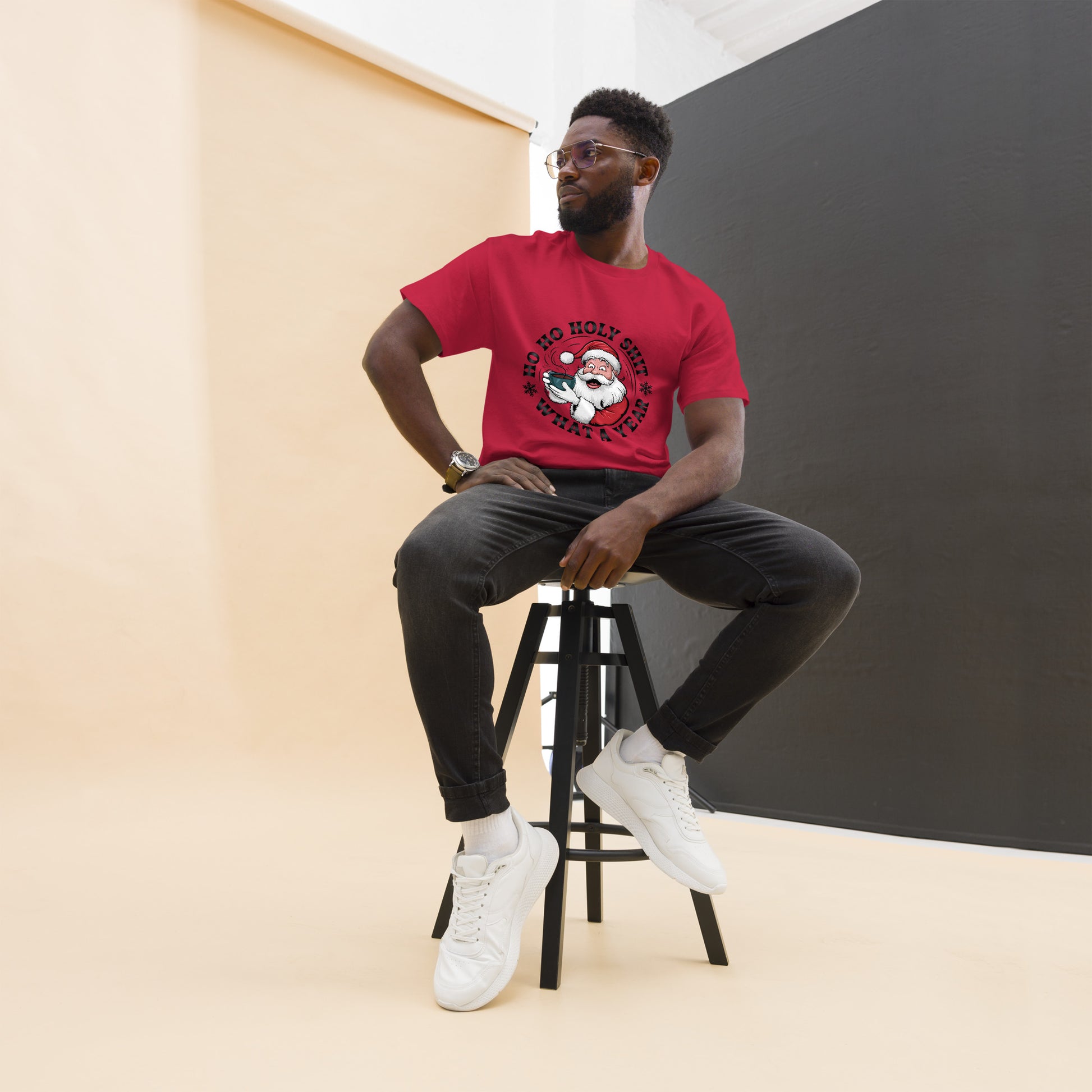 Man sitting on a stool wearing a red t-shirt with a graphic design, black pants, and white sneakers.