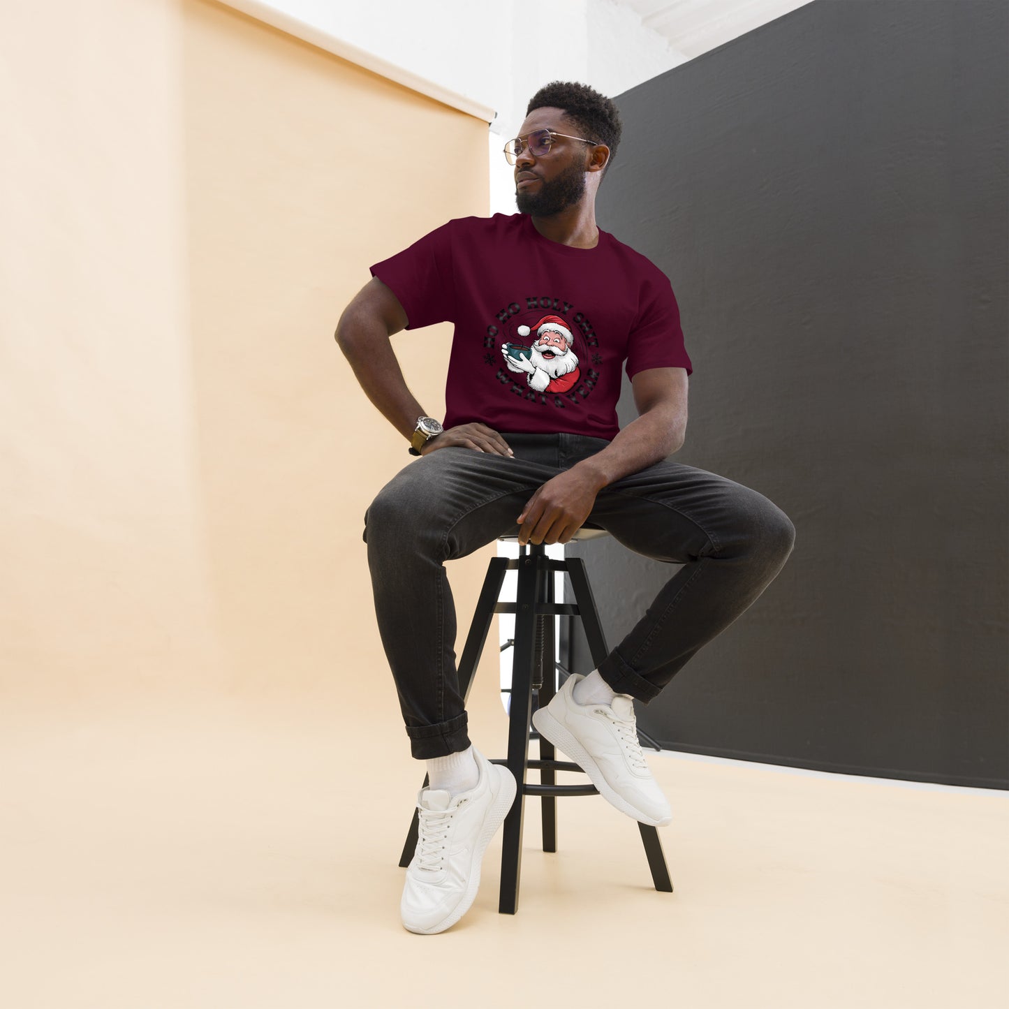 Man sitting on a stool wearing a maroon t-shirt with a graphic design, black pants, and white sneakers.