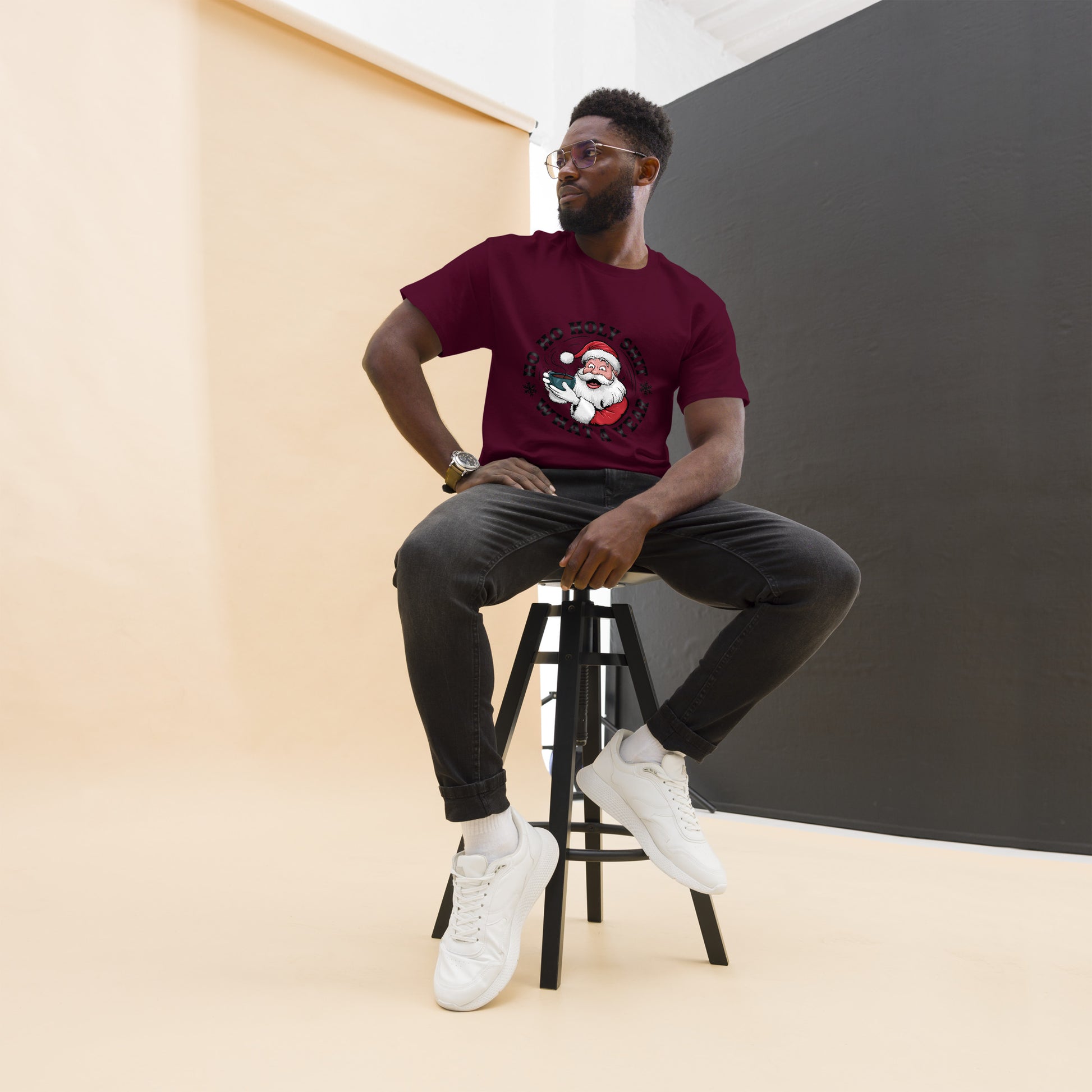 Man sitting on a stool wearing a maroon t-shirt with a graphic design, black pants, and white sneakers.